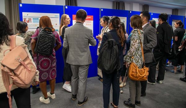 Conference attendees standing in front of poster boards, looking at the posters and talking to each other