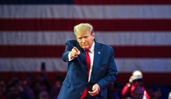 Donald Trump, pointing forwards, stood in front of an American flag