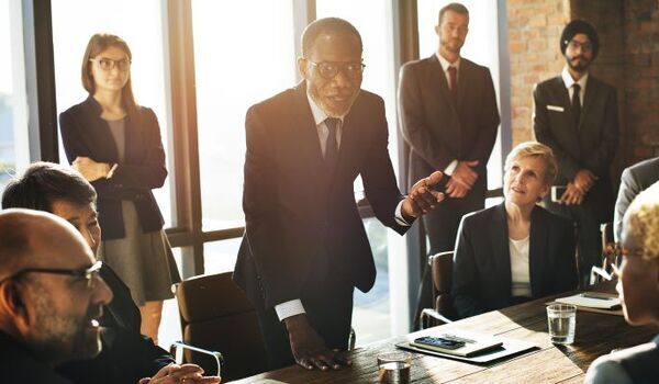 Office workers in suits sitting and standing round a table in a meeting