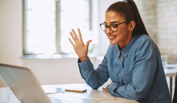 A person sat at a desk in front of a laptop, waving