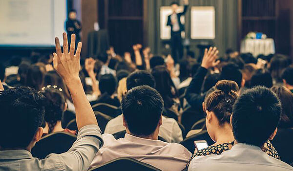 Crowd of people watching a presentation and raising their hands