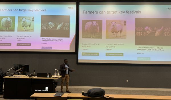 Dr Awal Fuesini presenting infront of his slides on a large screen