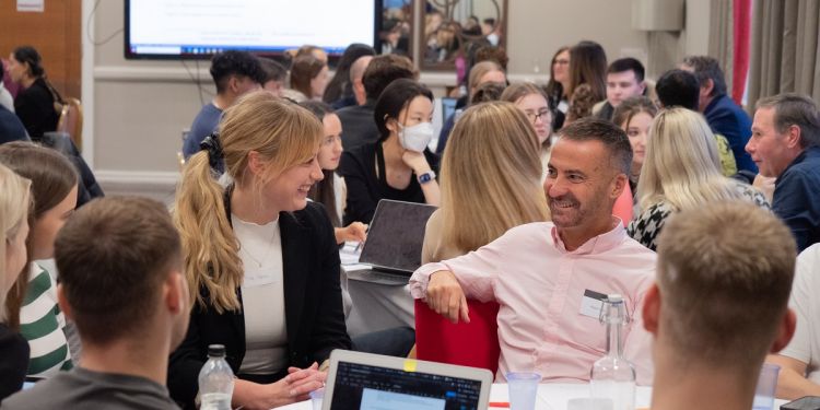 Two of our leaders are joined by a table of students. They are both smiling at each other and talking.