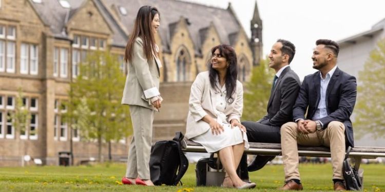 Four MBS students chatting on a bench in front of the Maurice Keyworth building.