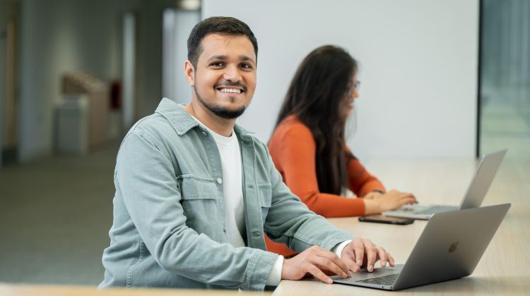 Two students using laptops in a modern building.