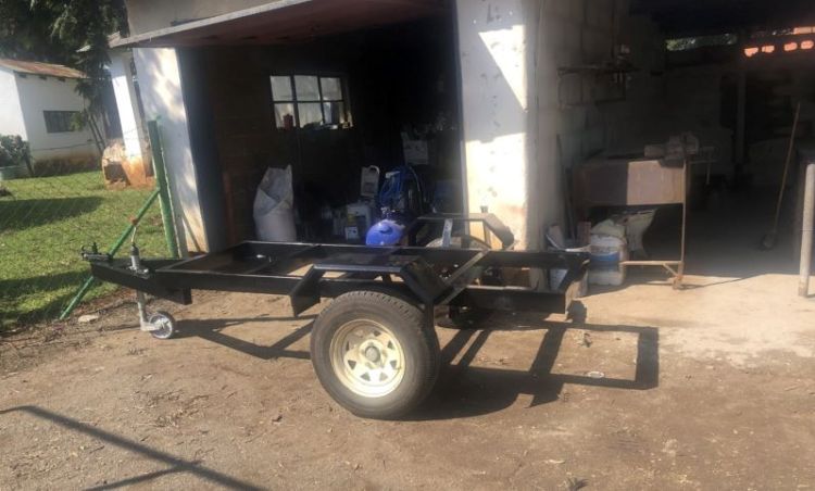 An empty trailer infront of a garage on a farm.