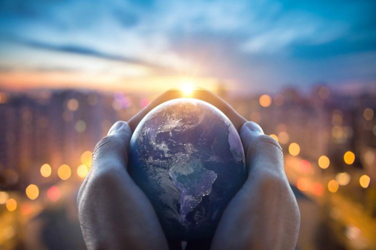 A globe is in the middle of the picture, held in between an unseen person's hands. In the background, the sun sets over a blurred cityscape.