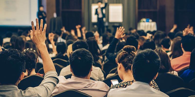 Crowd of people watching a presentation and raising their hands