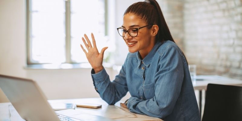 A person sat at a desk in front of a laptop, waving