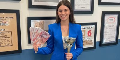 Sophie holds her cash reward and trophy whilst smiling.