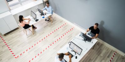 Four office workers sat apart at two desks with tape on the floor, marking out the distance