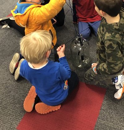 Children trying to pull obstacles on strings out of a bottle