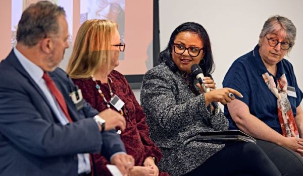 Three panel members looking at the fourth panel member who is speaking into a microphone