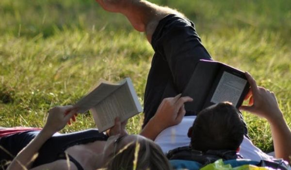 Man and woman relaxing on grass, reading books.