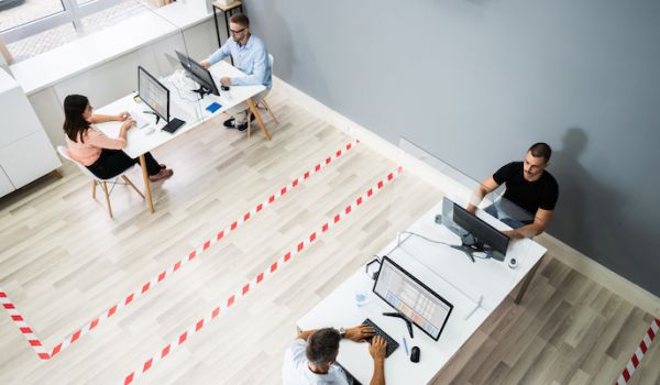 Four office workers sat apart at two desks with tape on the floor, marking out the distance