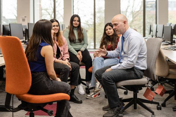 A lecturer speaks to a small group of students in a computer suite.