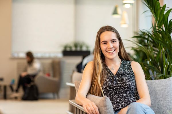 Student is sitting on a sofa, smiling to camera.