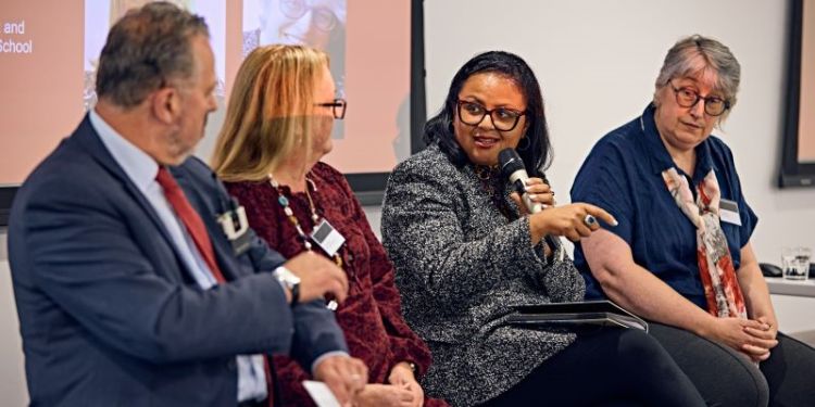 Three panel members looking at the fourth panel member who is speaking into a microphone