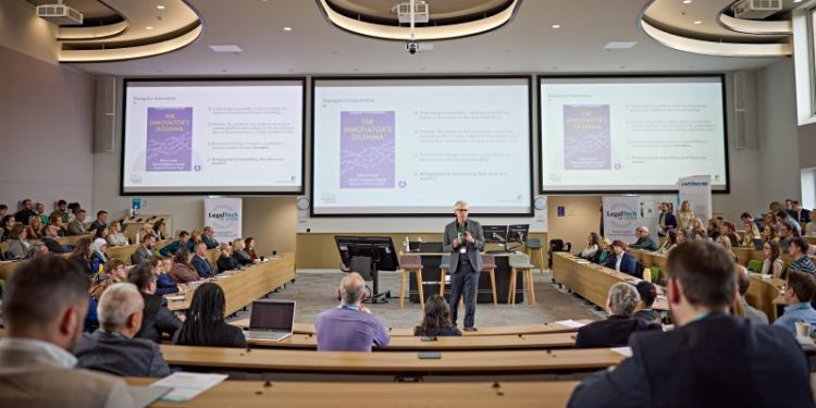 Person speaking into a microphone in front of an audience in a lecture theatre