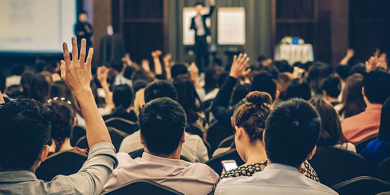 Crowd of people watching a presentation and raising their hands